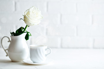 Gentle white rose in a vase and a cup of coffee. Selective focus. Background with copy space.