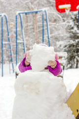 Little kid girl builds snowman on winter day outdoors.