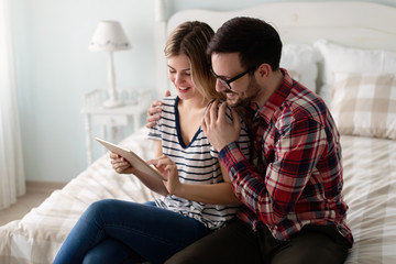 Young attractive couple using tablet in bedroom