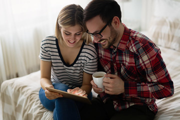 Young attractive couple using tablet in bedroom