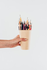 Close-up view of female hand holding cup with colorful pencils isolated on white background © LIGHTFIELD STUDIOS