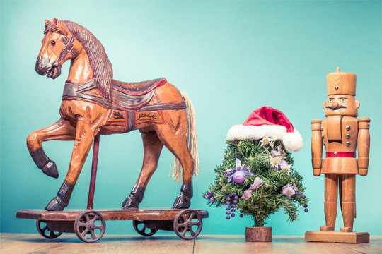 Retro antique Christmas wooden horse on wheels toy, old nutcracker and New Year tree in Santa's hat. Holiday greeting card. Vintage style filtered photo
