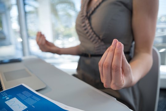 Mid section of female executive performing yoga at desk
