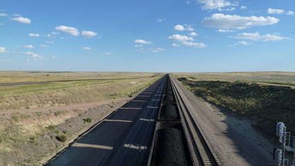 A long coal train passes through empty grasslands, blue sky and clouds, in the Powder River Basin of Wyoming, USA