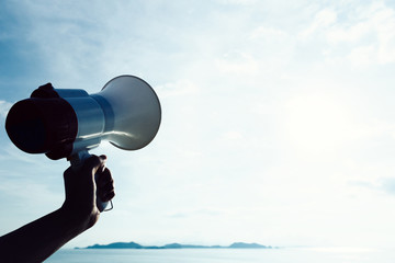 Hand hold megaphone against sea under sky background