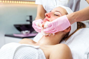Cosmetologist is doing Face peeling mask, spa beauty treatment for young girl. Model, close-up. Cosmetological clinic. Healthcare
