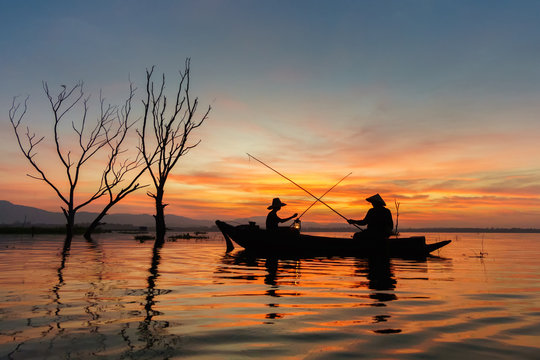 Silhouette asian fisherman, father and son fishing on a wooden boat in the river at sunrise.
