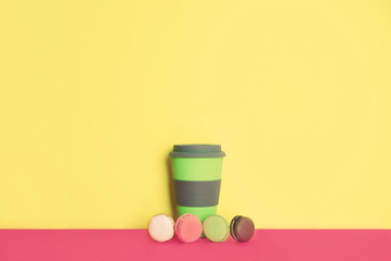 Cup of coffee to go with macaron on yellow and pink background