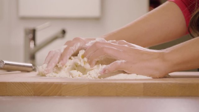 A woman kneads crumbly pastry dough on a kitchen counter - closeup - slow motion