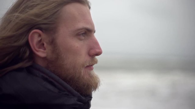 Portrait in profile of bearded caucasian guy being outdoor looking at storm dreaming about travelling or surfing feeling appeasement and solitude 