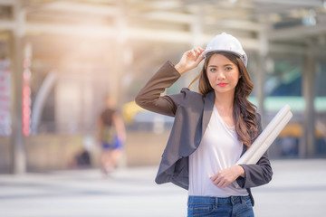 Portrait of Business woman wearing a helmet and holding drawing on blurred city background. Business planning concept.