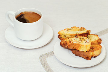 Italian homemade biscotti with nuts on white plate on tablecloth of fabric. Cantucci and coffee for breakfast. Selective focus. Copy space.