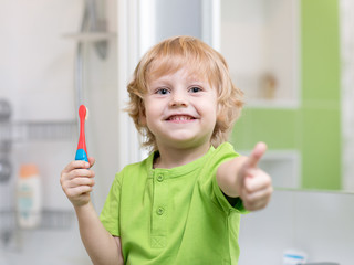 Little kid boy brushing his teeth in the bathroom. Smiling child holding toothbrush and showing...