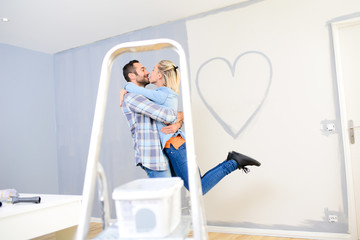 cheerful young love couple in new house painting decorating home and drawing a heart shape on the wall