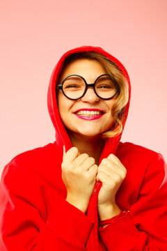 Portrait of young smiley student in black glasses in hood over pink background