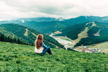 Fototapeta na wymiar girl, woman sitting sits on a hill and looks down at the beautiful view of the mountains and forests opening in front of her