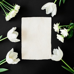 White flowers and paper card on black background. Modern composition. Flat lay, top view.