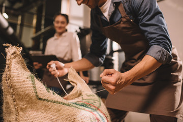 partial view of worker tying sack bag with coffee beans