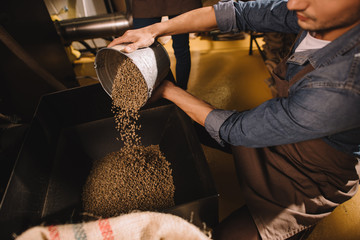 partial view of coffee roaster pouring coffee beans into roasting machine