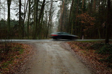 Rozmyta sylwetka samochodu na leśnej drodze na tle lasu. © W Korczewski