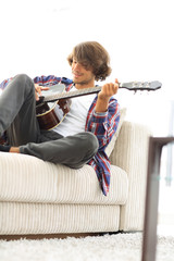 Handsome man playing on the guitar on the couch at home