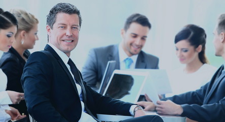 Portrait of mature business man smiling during meeting with colleagues in background