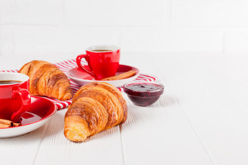Freshly baked croissant on napkin, cup of coffee in red cup on white wooden background. French breakfast. Fresh pastries for breakfast. Delicious dessert. Closeup photography. Horizontal banner