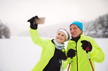 Senior couple with smartphone cross-country skiing.