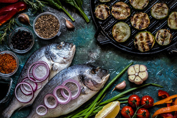 Dorada fish with vegetables, lemon, spices and greens on a blue background