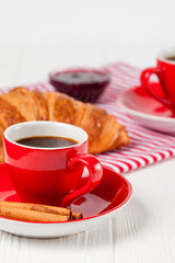 Freshly baked croissant on napkin, cup of coffee in red cup on white wooden background. French breakfast. Fresh pastries for breakfast. Delicious dessert. Closeup photography. Vertical banner