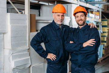 male workers in helmets hugging and posing in storehouse