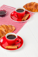 Freshly baked croissant on napkin, cup of coffee in red cup on white wooden background. French breakfast. Fresh pastries for breakfast. Delicious dessert. Closeup photography. Vertical banner