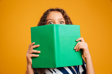 Excited shocked little girl child covering face with book.