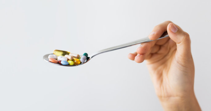 close up of female hand holding spoon with pills