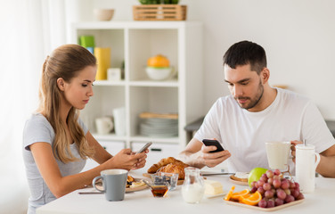 couple with smartphones having breakfast at home