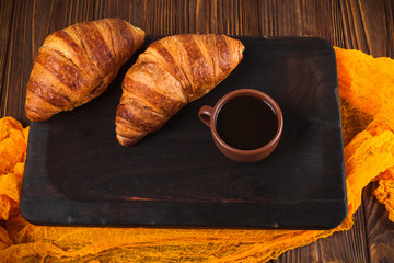 Freshly baked croissant jam, cup of coffee in white cup on brown wooden background. French breakfast. Fresh pastries for breakfast. Modern dark mood style. Delicious dessert. Horizontal banner