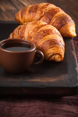 Freshly baked croissant jam, cup of coffee in white cup on brown wooden background. French breakfast. Fresh pastries for breakfast. Modern dark mood style. Delicious dessert. Vertical banner