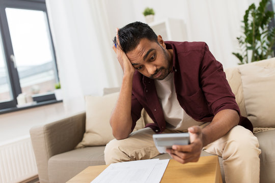 Confused Man With Papers And Calculator At Home