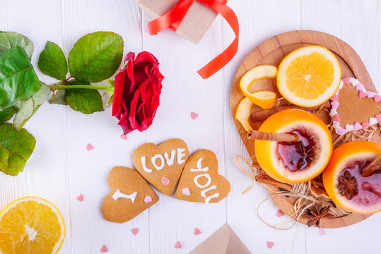 Festive composition with cookies in shape of heart with I Love you words, rose, unusual served in orange mulled wine on the white table. Valentine' s day surprize for lover. Selective focus.
