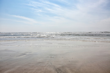 Sitting on the ocean beach, view at the waves in the sun with clouds in the sky