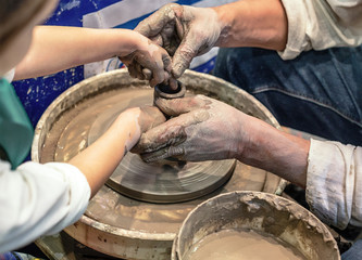 Pottery. A child and an adult with hands, smeared with clay, create a pot on the potter's wheel.