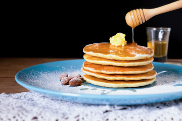 Pancakes with honey and almonds on blue plate for breakfast food on wooden table and black background.