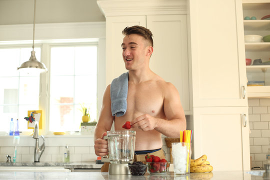 Young man with no shirt on making a healthy smoothie. 