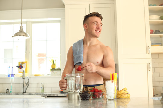 Young man with no shirt on making a healthy smoothie. 