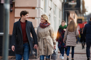 Portrait of young man and woman walking down the street and looking at each other with people on the background