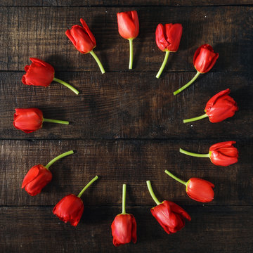 Round frame made of red tulips on dark wooden background