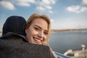 Fototapeta premium Sweet hug. Close up portrait of young woman cuddling man while laughing and looking at camera in open air. Copy space in right side