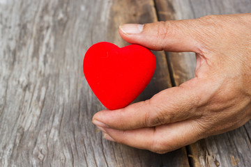 Old woman holding red heart shape decorate object in hand. Wooden background with copy space. Symbolic of love and Valentine event.