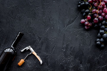 Uncorking the wine bottle. Bottle, corkscrew and bunches of red and black grapes on black...