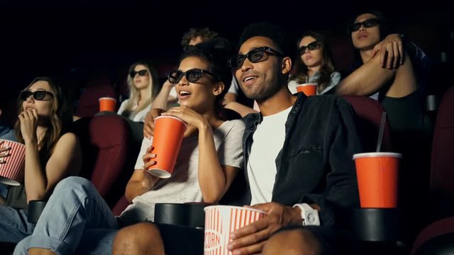 Pretty cheerful carefree couples in 3d glasses eating popcorn and watching movie in cinema